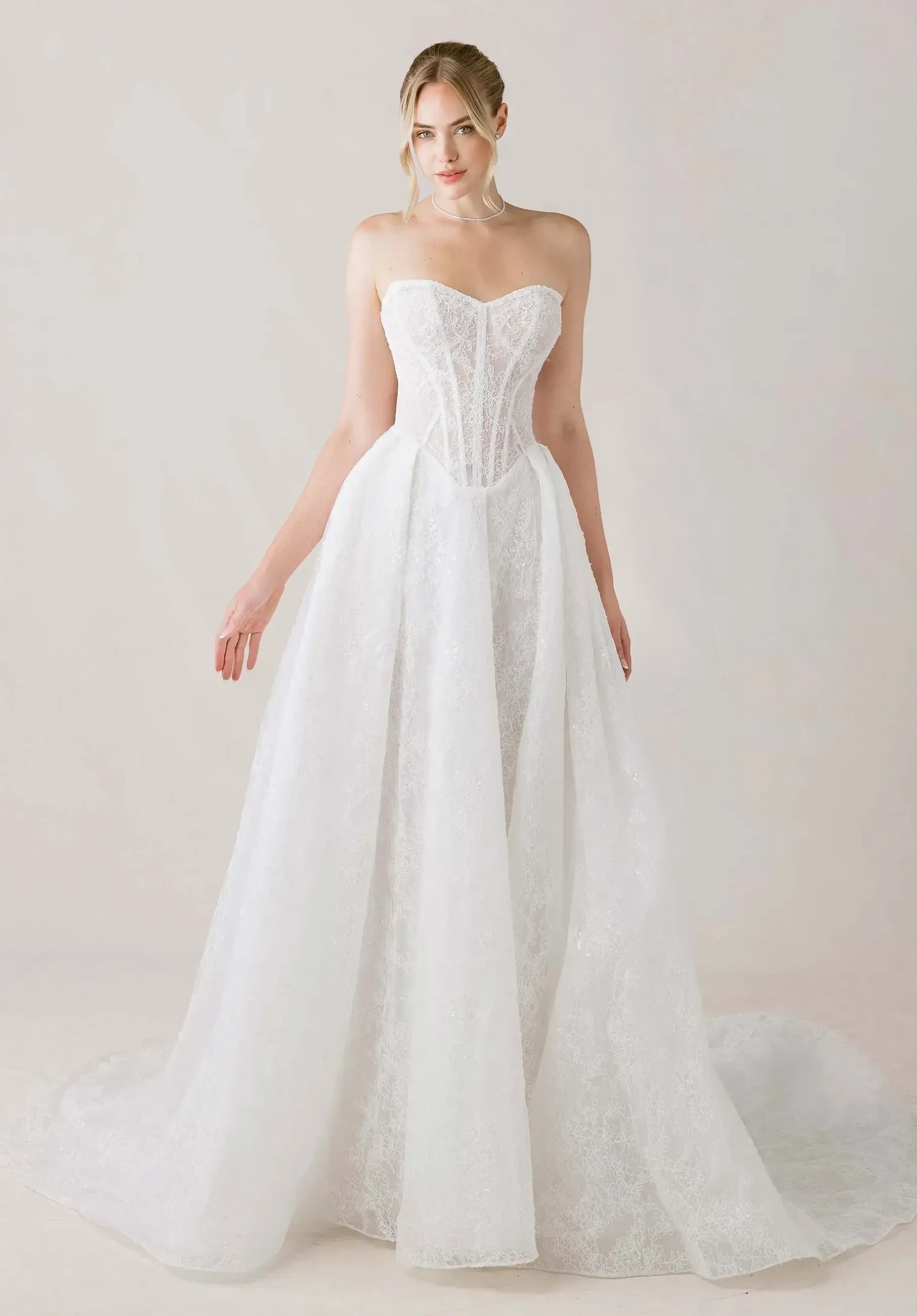 A woman in a strapless, white lace wedding gown stands gracefully. The dress features a fitted corset bodice and flowing skirt, conveying elegance and sophistication.