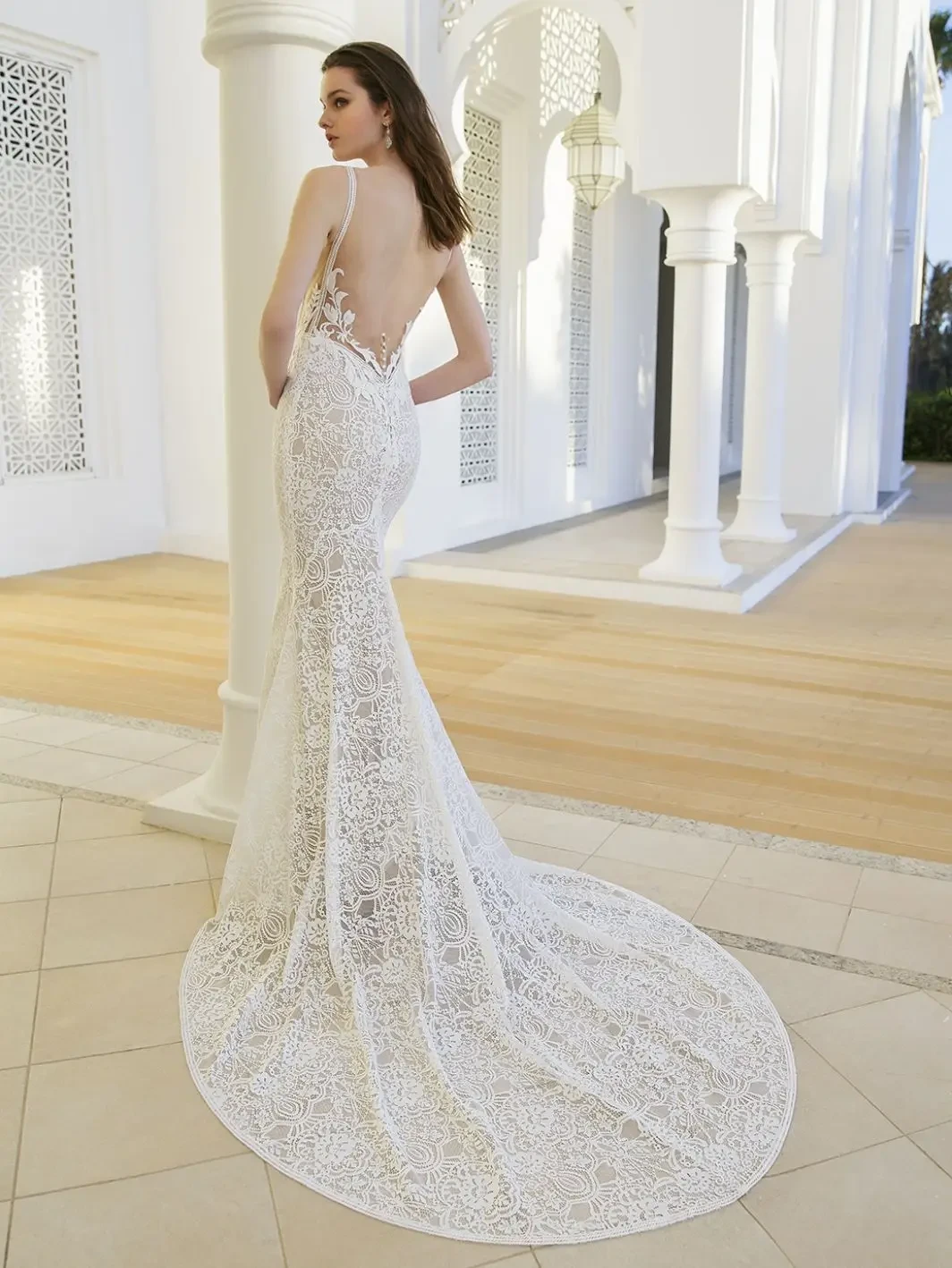 Model is wearing a deep V-neck lace gown with illusion side cut-outs, a sheer lace back, and a flowing train.