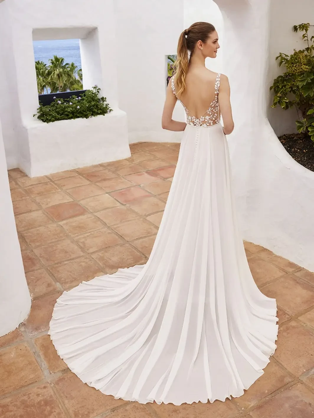 Model is wearing a chiffon gown with 3D lace details, a scoop neckline, illusion sides, and a low V-back.