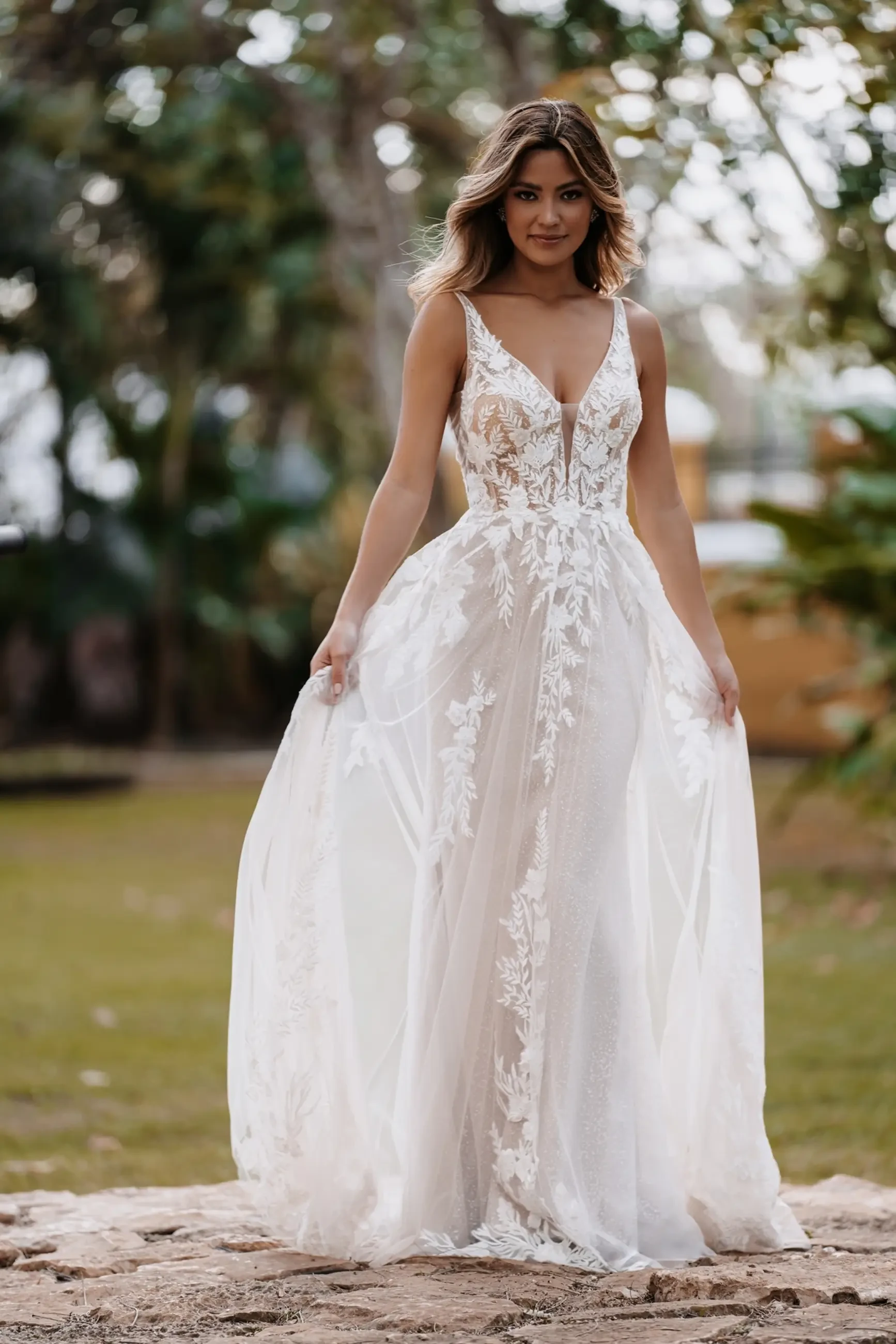 Model is wearing a sparkling A-line gown with sequined appliqués, a low scoop back, and layers of shimmering tulle