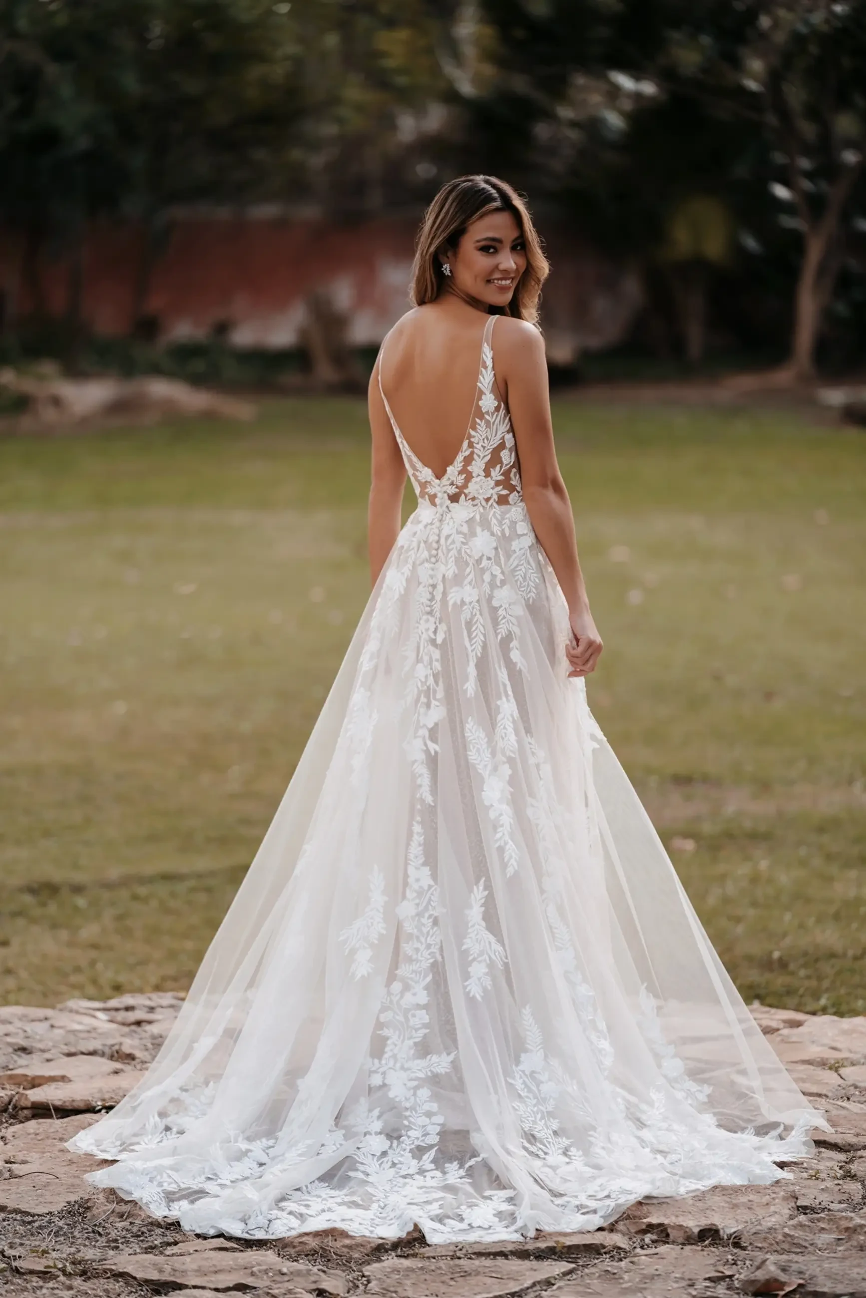 Model is wearing a sparkling A-line gown with sequined appliqués, a low scoop back, and layers of shimmering tulle