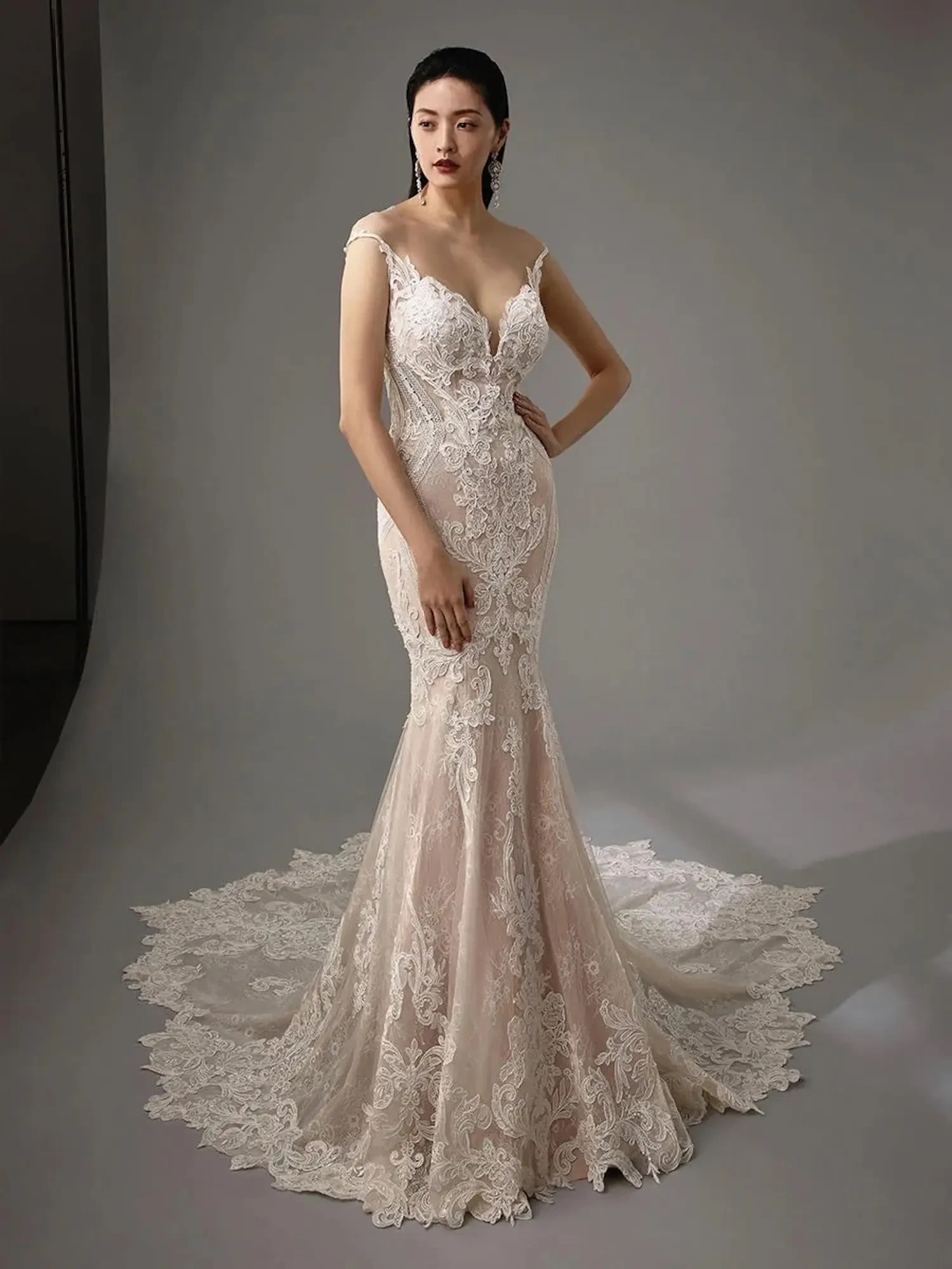 Model is wearing a trumpet silhouette gown with lace appliqués, a mermaid-inspired fit, and a flirty keyhole back for a sophisticated yet modern look.