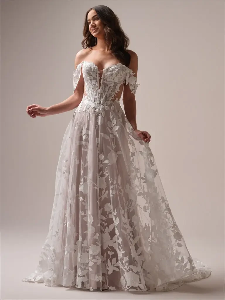 Woman in elegant off-the-shoulder wedding dress with floral lace overlay, smiling softly. The gown flows gracefully, creating a romantic, dreamy vibe.