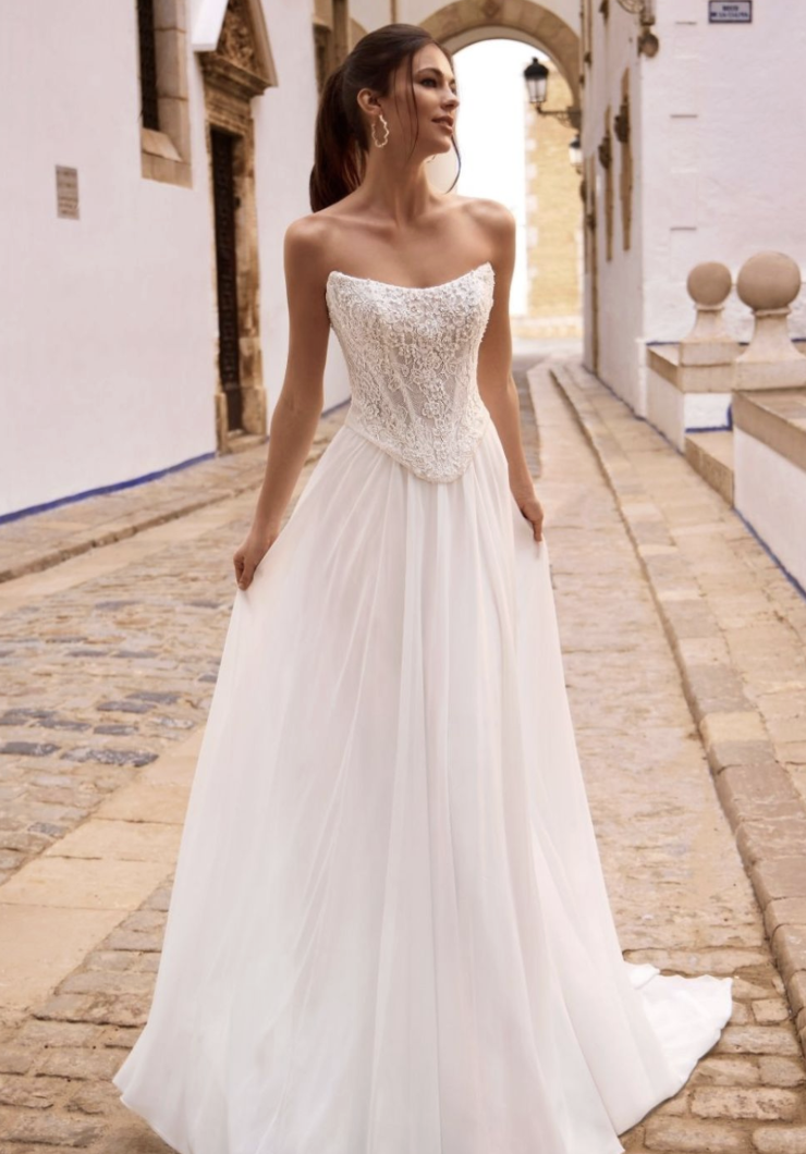 A woman in a white strapless wedding dress poses in a cobblestone street.