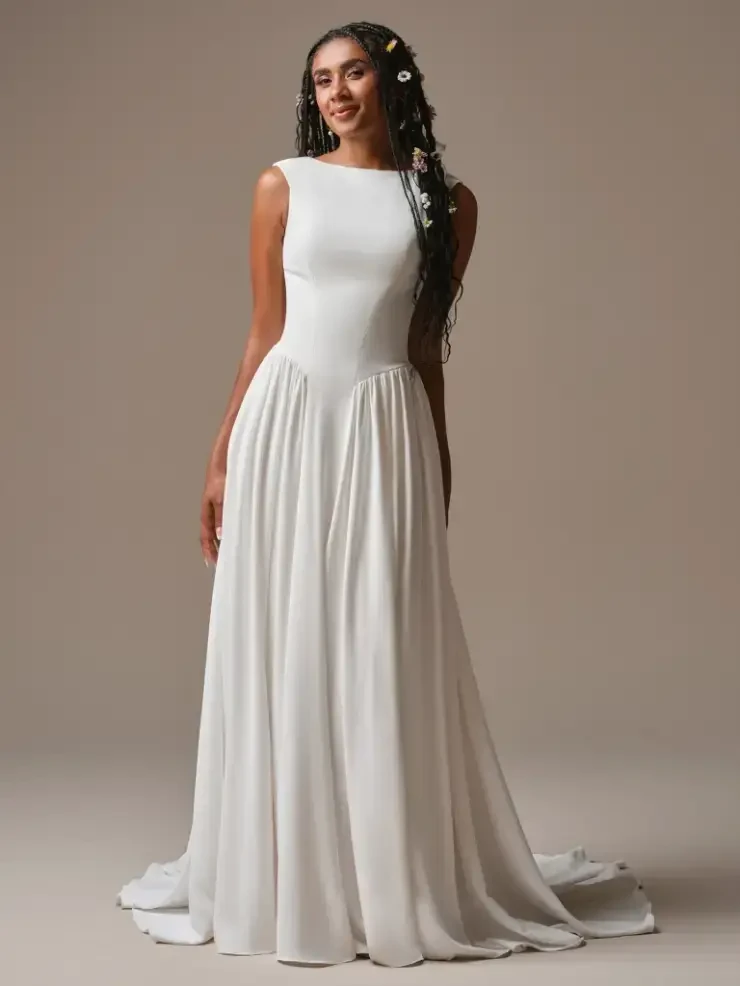 A model wearing a white, elegant dress with a fitted bodice and a flowing skirt, posed in a neutral setting.