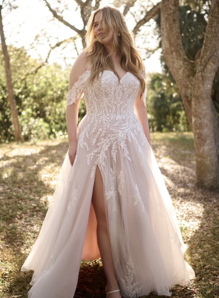A woman wearing a stunning wedding gown with intricate lace details and a thigh-high slit, standing outdoors in a natural setting with trees and soft lighting.